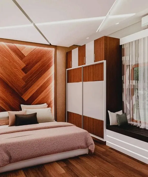 This bedroom design combines a warm, chevron-patterned wooden headboard with a practical two-tone sliding wardrobe and a cozy window seat, creating a perfect blend of style and comfort.