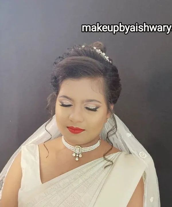 A beautiful Christian bride in a classic white saree and veil. The makeup is soft and luminous, with a bright red lip for a pop of color, and the hair is styled in an elegant updo.