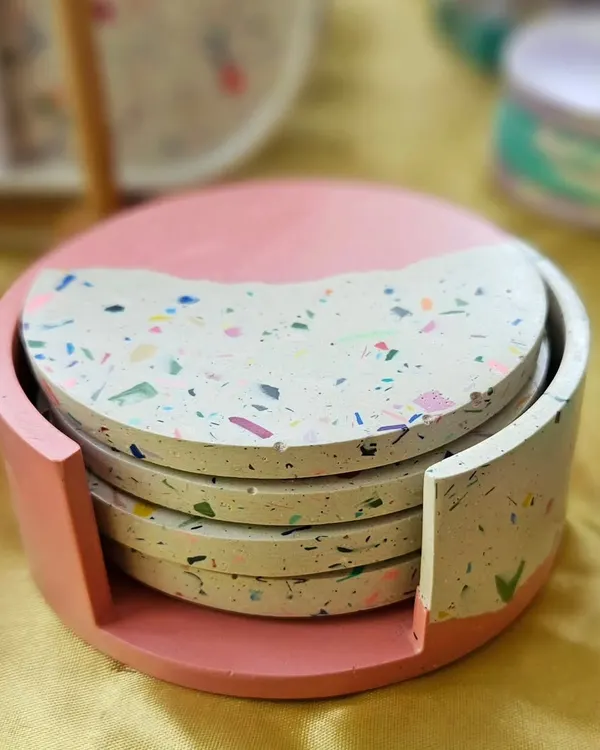 A set of four terrazzo coasters with a matching holder. This set features a half-pink, half-terrazzo design, making it a unique and functional piece of home decor.