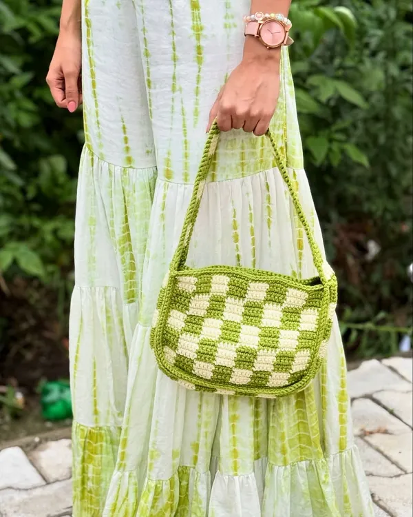 A full view of our handmade checkered crochet bag in a vibrant lime and white pattern, held against a matching tie-dye dress to show how it completes a look.