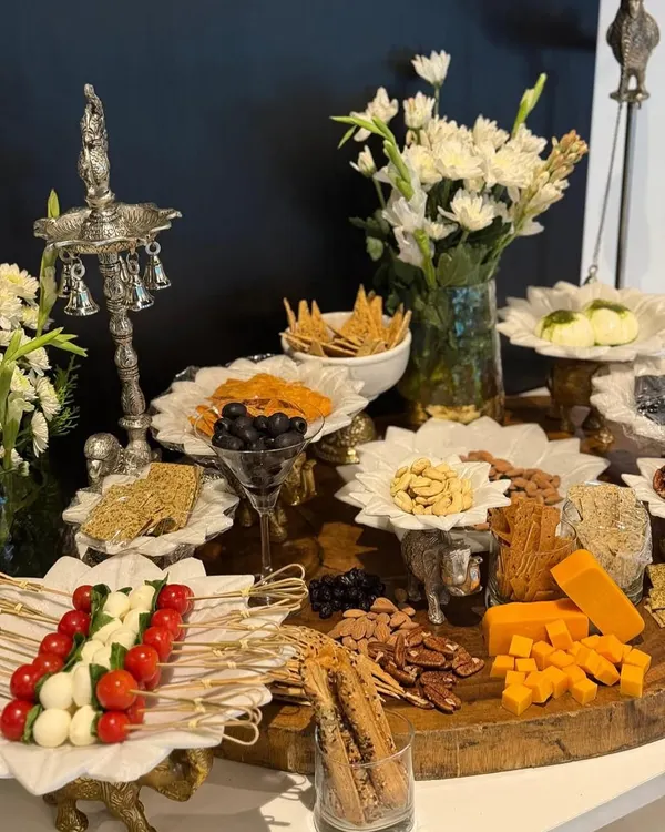 This is what my 'ishq' for food looks like on a table. A beautiful spread featuring a variety of gourmet cheeses, fresh Caprese skewers, assorted crackers, nuts, and olives, all styled with elegant silverware and fresh white flowers to create a true feast for the eyes.
