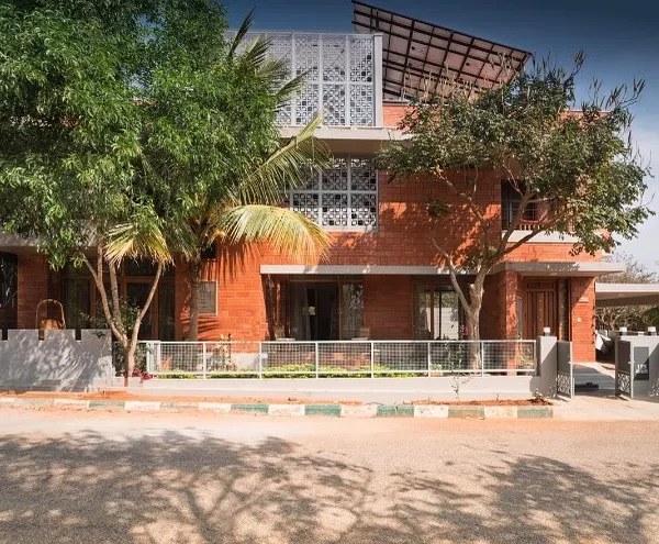 The Reshma Residence in Bangalore showcases a modern facade combining exposed brick with clean concrete lines and protective jaali screens. The design thoughtfully integrates mature trees on the plot, making the home feel connected to its environment.