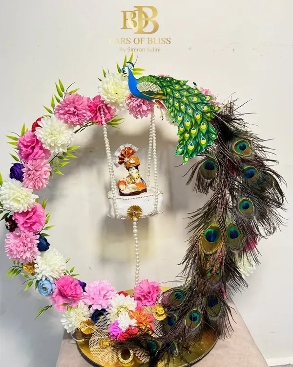 My most elaborate Janmashtami Jhula hamper. This design features a floral and peacock feather wreath around a swinging Ladoo Gopal, with a base of treats below.