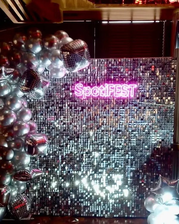 For the 'SpotiFEST' corporate event, we designed this high-impact photo wall featuring a shimmering silver sequin backdrop and a custom neon sign with the event's branding. This setup creates a modern, shareable experience for guests.