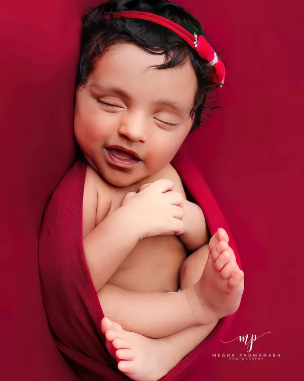 A dreamy smile from a newborn snugly wrapped in a rich red swaddle. We focus on capturing these fleeting expressions that reveal your baby's budding personality.