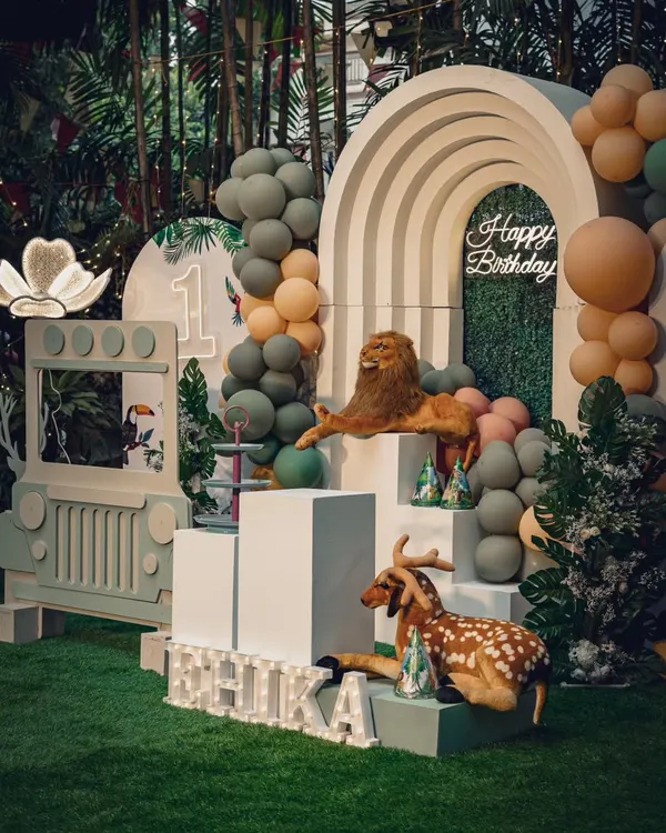 A sophisticated safari theme for a first birthday. This setup uses a beautiful rainbow arch, a green hedge backdrop, and realistic animal props to create a chic and wild celebration.