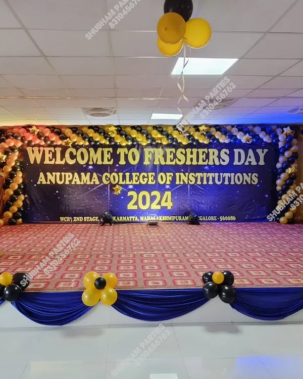 A grand stage decoration for a college Freshers Day, with a large banner and a black and yellow balloon arch.