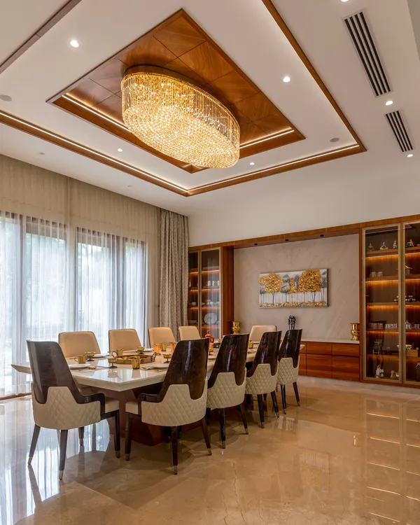 This luxurious dining room features a ten-seater marble table, a stunning crystal chandelier, and a custom-built wooden crockery unit, creating an elegant space for formal gatherings.