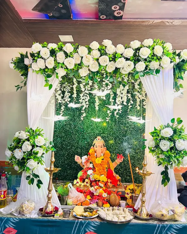 This is one of my most requested modern Ganpati decoration setups. It features a lush green grass panel backdrop, elegant white drapes, and arrangements of artificial white roses, creating a serene and sophisticated space for the festival.