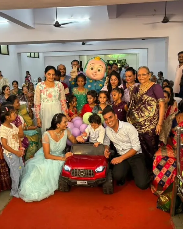 A wonderful group photo capturing the joy of a mascot appearance. The popular Cocomelon character stands among the children and family, posing for a picture after the birthday boy's grand car entry.
