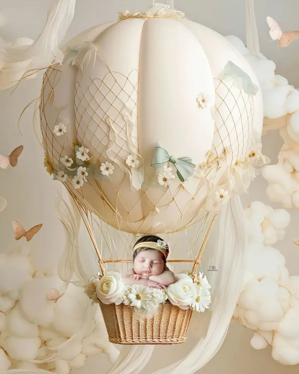 A dreamy newborn portrait featuring a baby sleeping peacefully in a miniature hot air balloon basket, surrounded by soft, cloud-like props. This fine art newborn photography showcases my love for creating magical, imaginative scenes.