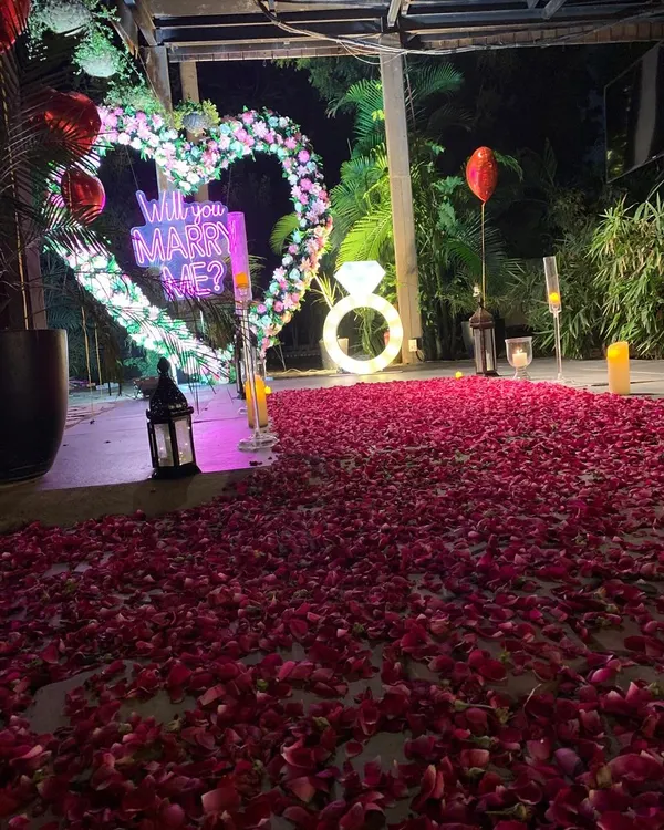 A close-up view of our popular outdoor proposal decoration. The glowing "Will You Marry Me?" sign and illuminated ring prop are perfectly framed by a floral heart, creating a picture-perfect setting.