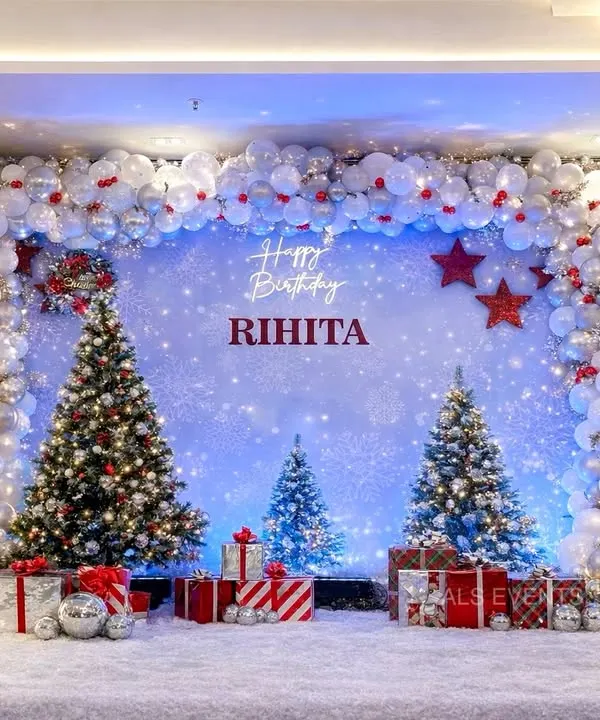 An elegant "Winter ONE-derland" theme for Rihita's first birthday. The stunning balloon arch is filled with white, silver, and red ornaments, framing a backdrop of sparkling snow and decorated Christmas trees.