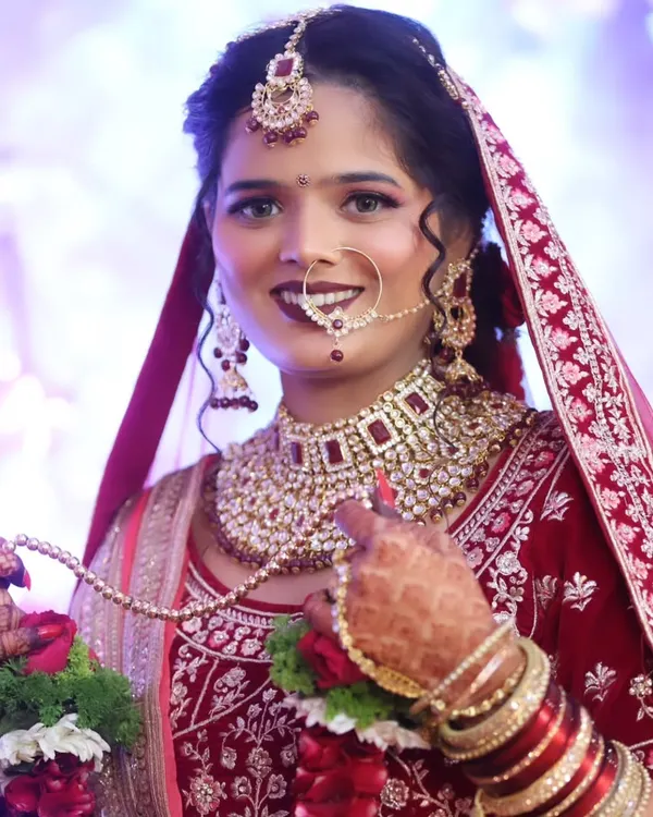 A classic North Indian bridal look, focusing on radiant skin, bold eyes, and a deep red lip that complements the intricate velvet lehenga. This is all about creating a timeless, royal elegance for your big day.