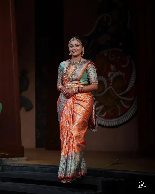 A stunning full-length portrait of a South Indian bride in her gorgeous orange and teal Kanjeevaram saree. We take the time to capture these elegant shots that showcase the entire bridal look.