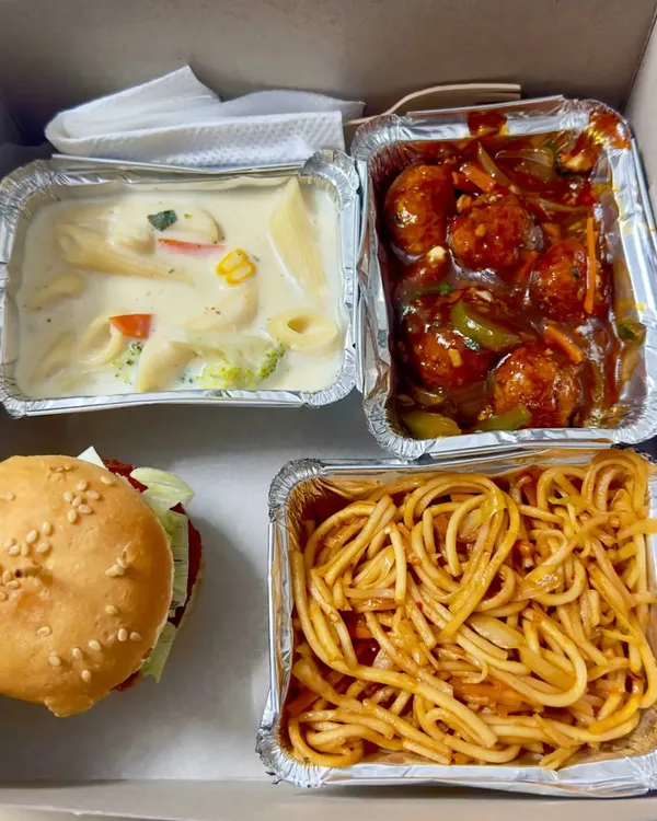 A look inside one of my popular multi-cuisine snack boxes. This one features a veg burger, white sauce pasta with broccoli, spicy veg manchurian, and hakka noodles, perfect for someone who loves variety.