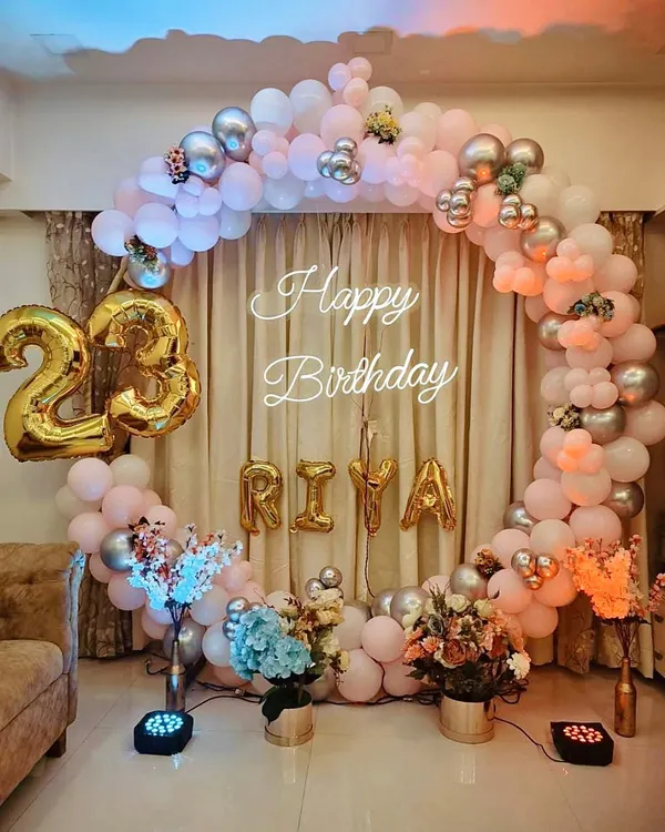 A beautiful circular balloon arch in pastel pink, peach, and silver for a 23rd birthday. The setup includes foil number balloons for the age and the birthday girl's name "RIYA" for a personalized touch.