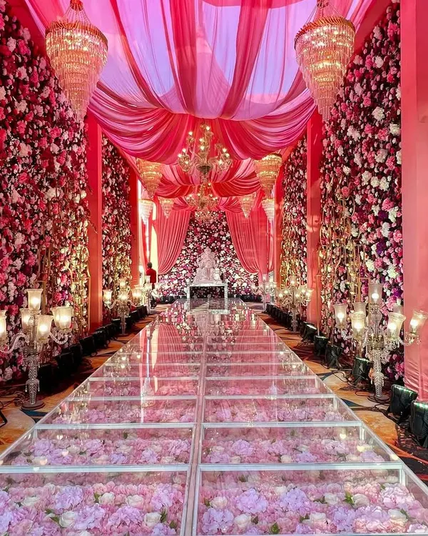 Walking on a path of flowers. This stunning glass aisle filled with pink hydrangeas, surrounded by floral walls and elegant chandeliers, creates a true fairytale entrance for the bride and groom.