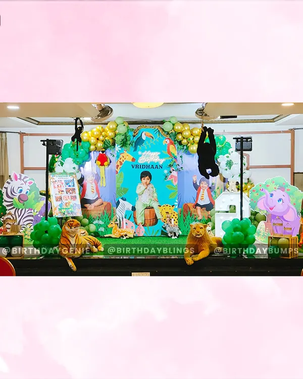 A wide view of our grand jungle-themed birthday stage, complete with a personalized backdrop, numerous animal props like a tiger and giraffe, and an expansive balloon arch in green and gold.