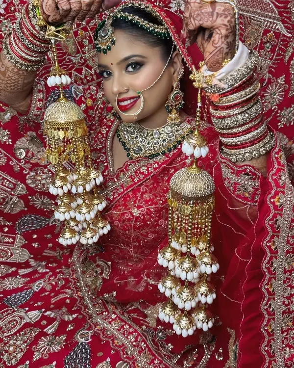 A classic bridal pose, showing off the beautiful kalire against a vibrant red lehenga. The makeup features a bold red lip and defined eyes to match the traditional attire.