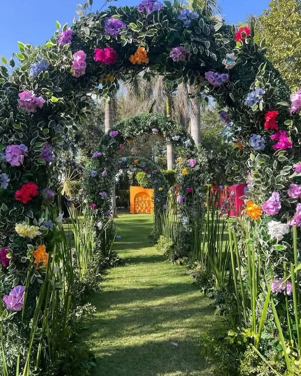 A magical garden entrance featuring a series of arches covered in lush greenery and colorful flowers, creating an enchanting tunnel for guests to walk through.
