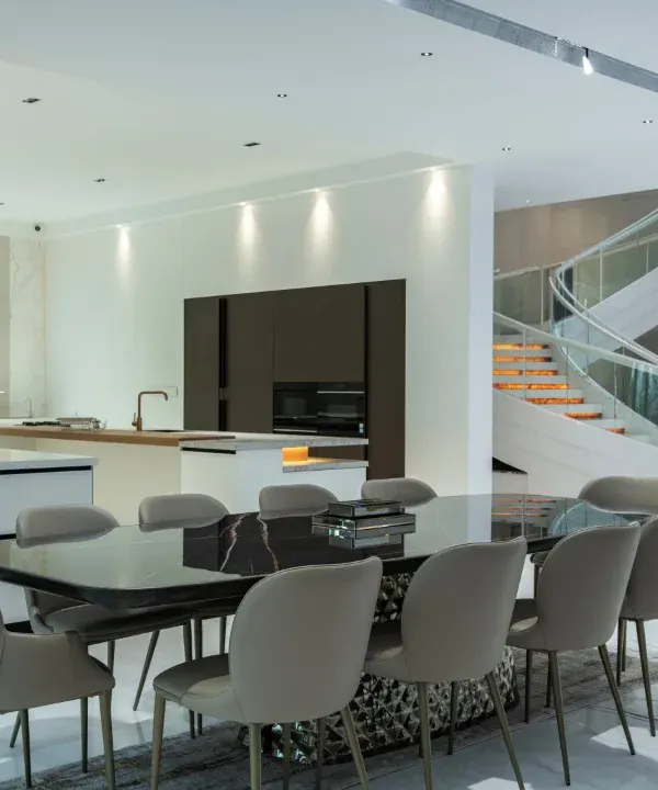 A space that speaks for itself. This open-plan dining area is defined by its clean lines, marble flooring, and the magnificent sweep of a sculptural staircase, creating a dialogue between modern luxury and spatial fluidity.