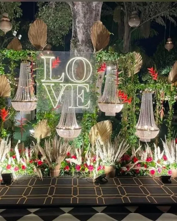 This stunning boho-glam photo spot is a perfect example of how I blend different styles. The neon 'LOVE' sign adds a modern touch to the rustic arrangement of pampas grass, dried palms, and elegant chandeliers, creating a memorable backdrop for an anniversary or engagement party.