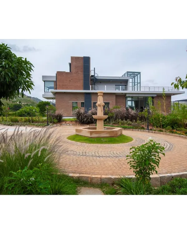 The grand entrance to our weekend home at Nandi Hills, featuring a circular driveway and a central water fountain. The landscape design uses native grasses and trees to frame the contemporary brick building, creating a welcoming approach.