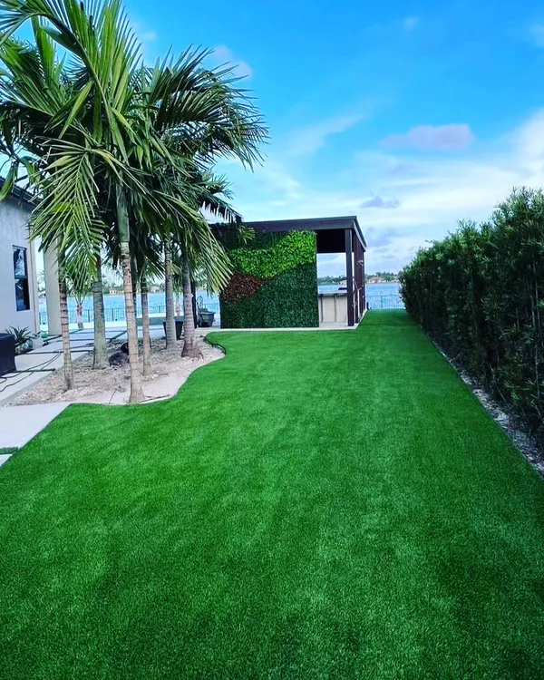 A large backyard with a complete artificial turf installation. The grass extends from the patio to a hedge and a separate cabana area, creating a seamless, clean green space.