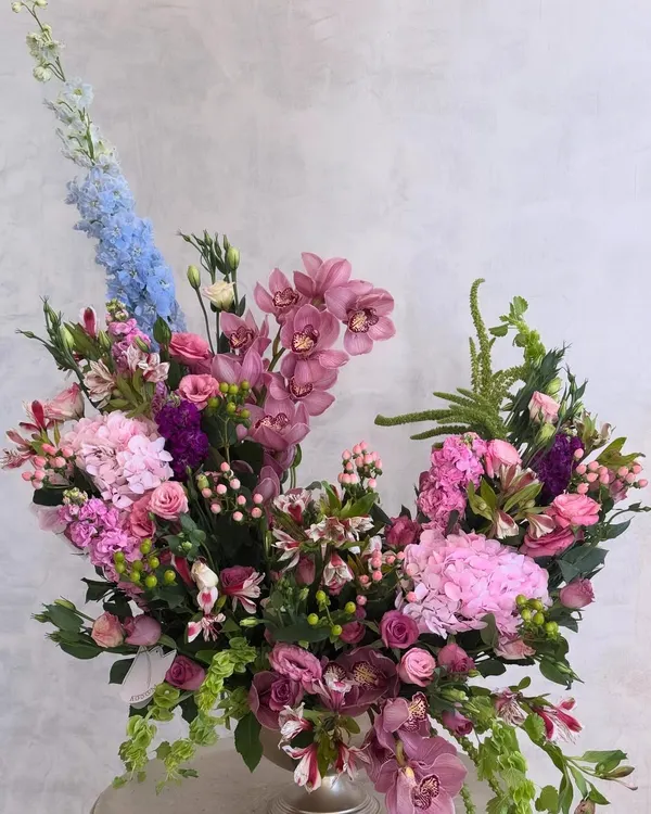 This arrangement is an expression of Wabi Sabi, the beauty of imperfection. The asymmetrical shape and mix of textures, from soft hydrangeas to tall delphiniums and exotic orchids, create a piece that is poetic and unique.