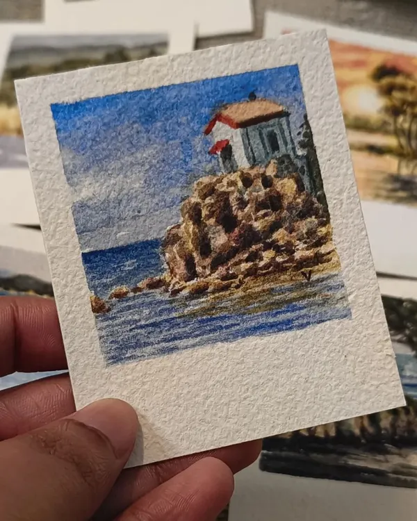A miniature watercolor painting of a solitary lighthouse perched on a rocky cliff by the sea. The details in the stonework and the deep blue of the water make this a captivating little coastal scene.