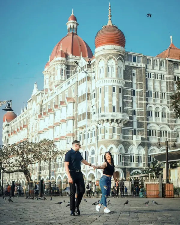 A classic Mumbai pre-wedding shot. The couple walks hand-in-hand in front of the magnificent Taj Mahal Palace Hotel, creating an iconic and timeless memory.