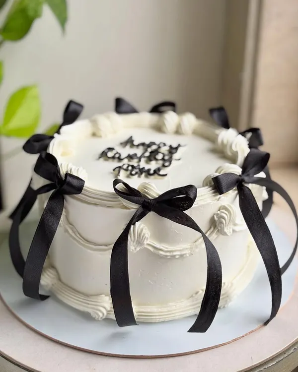 A full view of the balletcore-inspired cake, showcasing the classic piped swirls and the elegant arrangement of black satin bows around the sides and top.