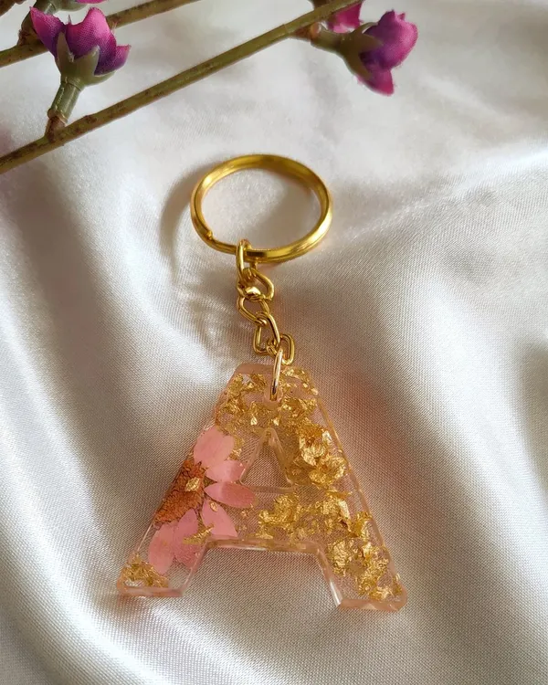 Initial keychains are a wonderful personalized gift. This 'A' keychain is made with light pink flower petals and shimmering gold flakes, creating a unique accessory that is handmade with love.