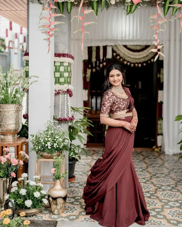 A modern reception look featuring a custom-made fish-cut skirt in a deep maroon. The skirt is paired with an embroidered blouse and a draped dupatta, elegantly cinched at the waist with a belt to create a sophisticated and contemporary silhouette.