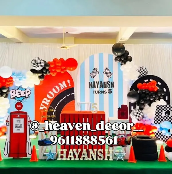 An epic Disney Cars themed 5th birthday party featuring Lightning McQueen. The large-scale setup includes multiple themed backdrops, a gas pump prop, and character cutouts, creating a full racetrack scene.