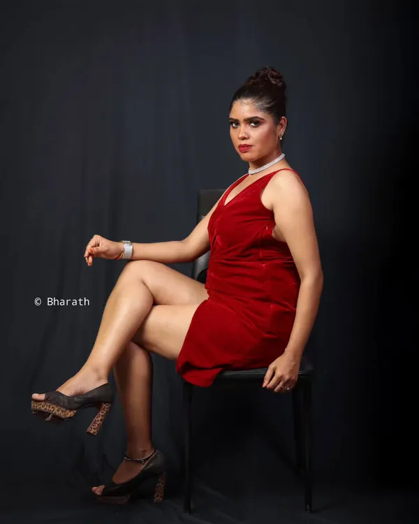 A classic studio portrait of a model in a velvet red cocktail dress. The seated pose is powerful and confident, and the dark background makes the red fabric stand out.