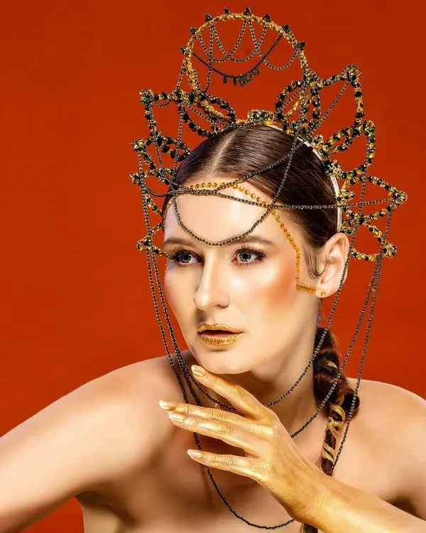 An editorial fashion portrait of an international model wearing an elaborate, artistic headpiece against a bold red background. This showcases our ability to execute high-concept, creative shoots for fashion magazines and campaigns.