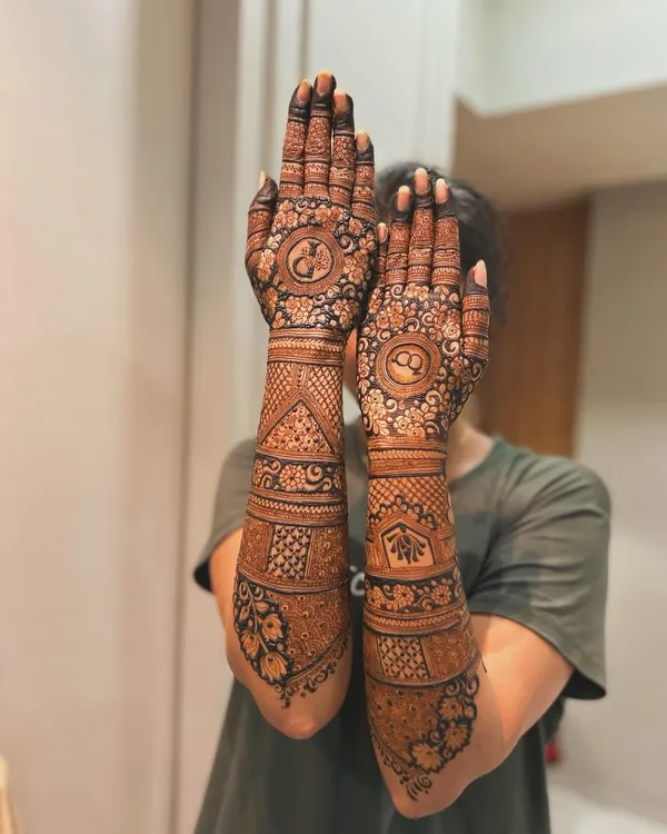 A beautiful, full-arm bridal design for an engagement ceremony. The design includes personalized initials and traditional motifs, covering the hands and forearms completely.