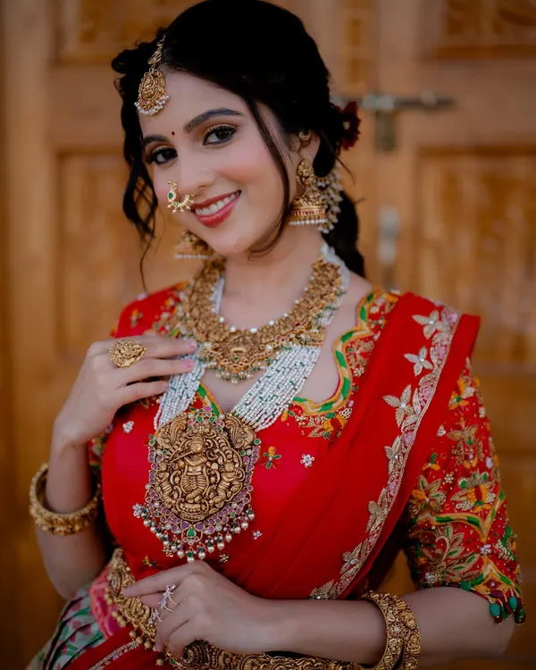 A radiant bridal portrait. The bride's joyful smile and the stunning details of her red half saree and temple jewellery are captured perfectly in the soft, natural light.