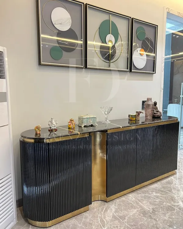 This modern console unit is a statement piece, featuring a fluted black wood finish, a black marble top, and a striking asymmetrical design with a polished gold-finished accent.