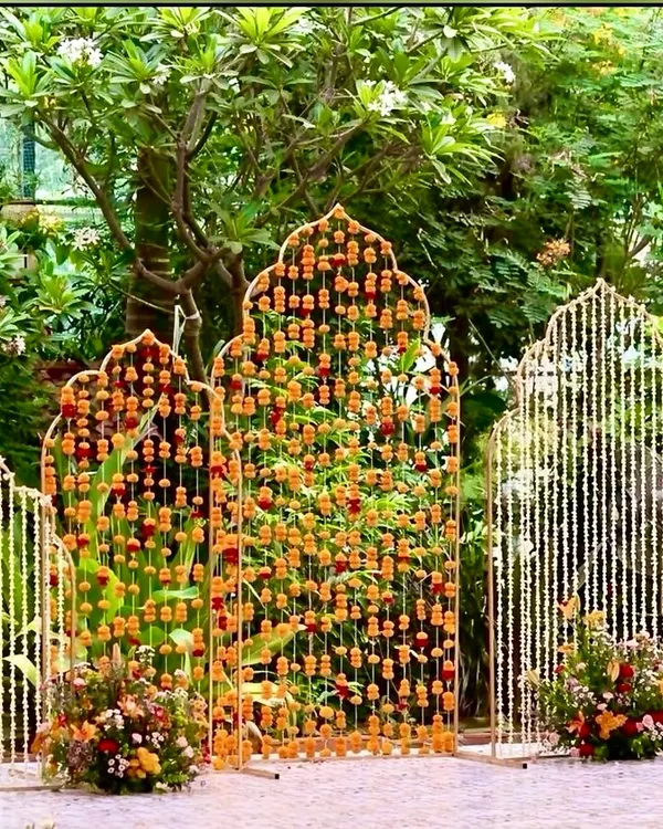 This modern Haldi backdrop features arched panels intricately decorated with marigold and tuberose garlands. It's a fresh take on traditional floral decor, creating a stunning focal point for your ceremony.