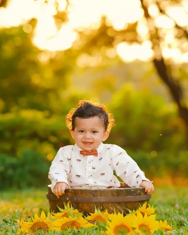 A beautiful golden hour portrait of a toddler in a rustic barrel surrounded by sunflowers. The warm, soft sunlight creates a magical glow, perfect for outdoor kids photography.