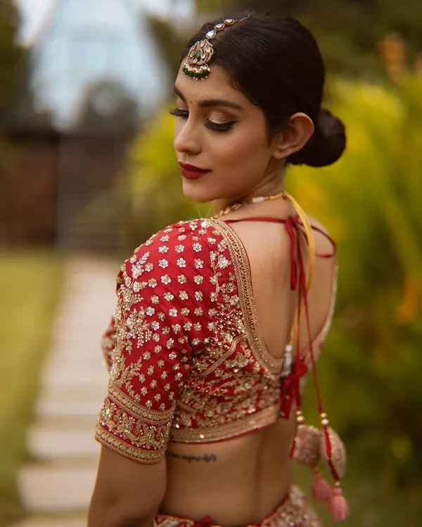 A truly royal bridal look. The deep red lip and defined eyes perfectly complement the exquisite embroidery of the red lehenga and the traditional back details.