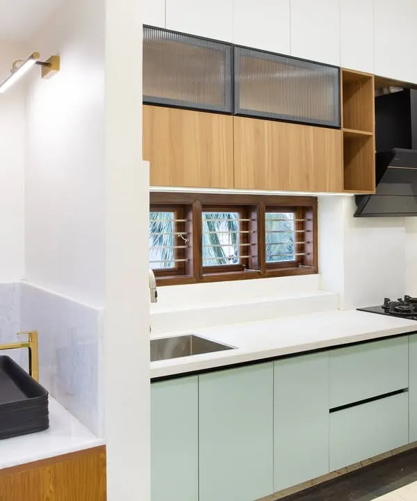 A view from the side, showing the main L-shaped kitchen workspace. The combination of matte sage green lower cabinets and wood-look uppers with fluted glass creates a soft, layered look that is full of texture and interest.
