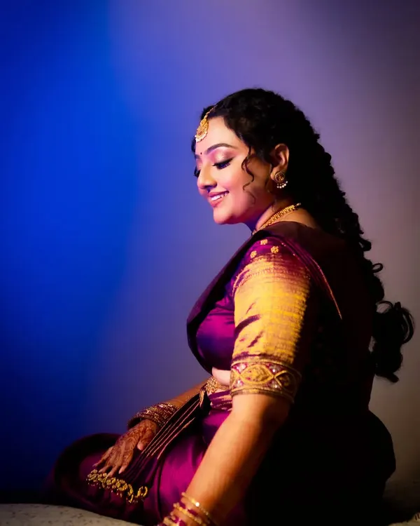 A creative bridal portrait using a mix of blue and purple light. The vibrant colors and her serene, smiling profile create a dreamy and artistic image.