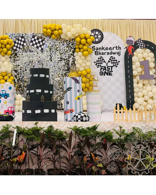 A full view of the "Fast One" racetrack-themed first birthday party. The setup includes a custom cake table, a backdrop with road graphics, and balloon arrangements, creating a fun and dynamic environment for the celebration.