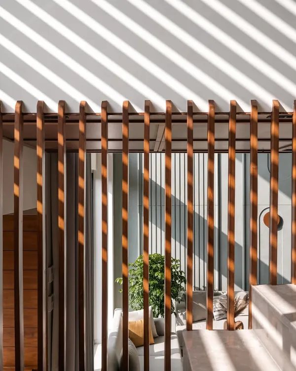 The play of light and shadow is a key element in our designs. In Amber House, the afternoon sun streams through the vertical wooden railings, casting graphic patterns on the walls and floor, transforming the architectural structure into a living piece of art.