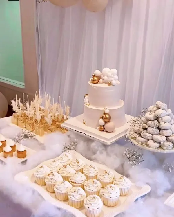 A closer look at our dreamy, all-white dessert table. The two-tiered cake is adorned with delicate sugar bubbles, surrounded by a cloud of white fabric and a variety of coordinated white and gold desserts.