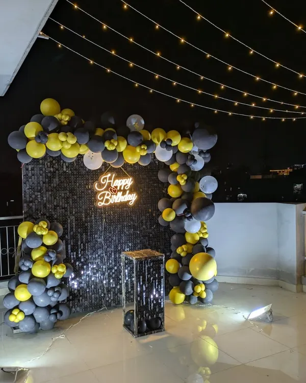 This is how I transform a simple terrace into a glamorous party spot. The setup features a black sequin shimmer wall, a stylish yellow and grey balloon arch, a custom neon sign, and a canopy of fairy lights to create the perfect ambiance for an unforgettable night.